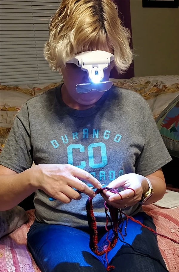 A customer crocheting with both hands while wearing the VisionAid, its LED light shining on her work